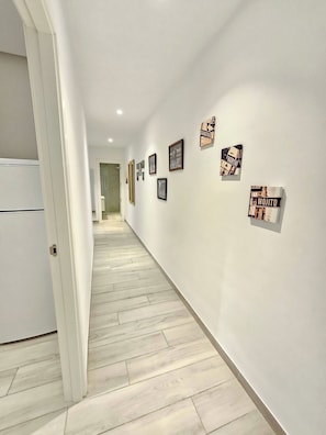 Un pasillo con un refrigerador blanco a la izquierda, piso de madera y varias fotografías enmarcadas en la pared.