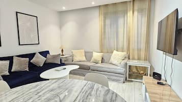 Una sala de estar moderna con una mesa de comedor de mármol, un conjunto de sofás, un televisor y una lámpara de techo.