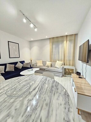 Una sala de estar moderna con una mesa de comedor de mármol, un conjunto de sofás, un televisor y una lámpara de techo.