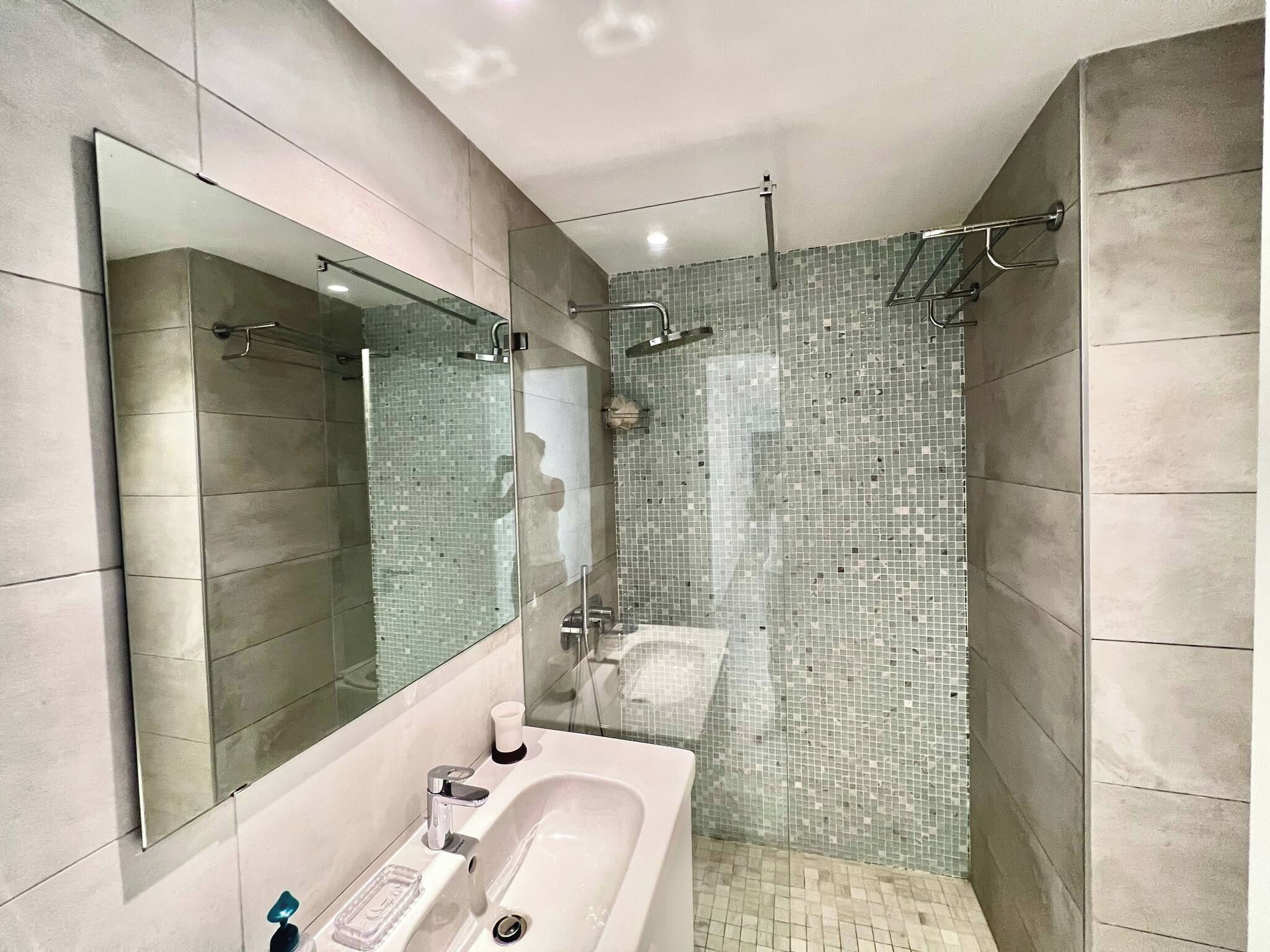 Un baño moderno con un espejo grande, una bañera y una zona de ducha con mosaicos.