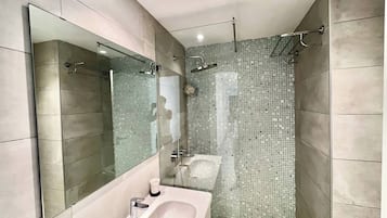 Un baño moderno con un espejo grande, una bañera y una zona de ducha con mosaicos.