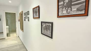 A hallway with framed black and white photographs on the walls, a wooden floor, and a door leading to a bathroom.