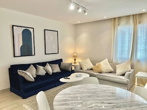 A modern living room with a dark blue sofa, a round marble coffee table, and two couches with light-colored cushions. - Luminous Escape to La Marsa (La Marsa)