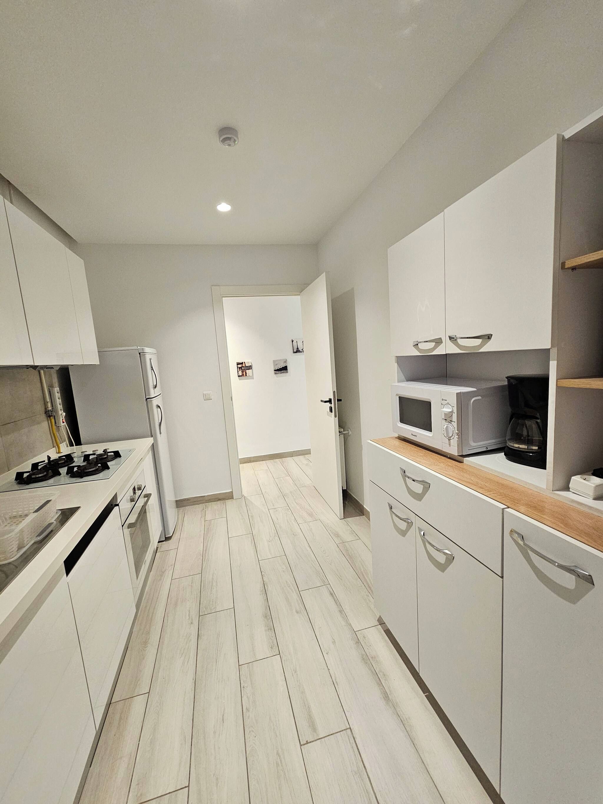 Una cuina moderna amb armaris blancs, fogó de gas, microones i cafetera.