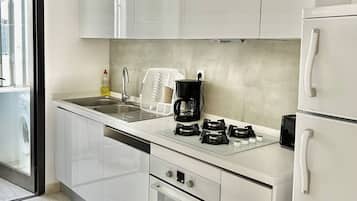 A modern kitchen with white cabinetry, a built-in dishwasher, a coffee maker, and a stove.