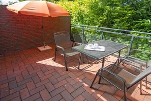 A patio with a table and chairs, an umbrella, and a brick wall. - Holiday apartment with 1 bedroom (Bensersiel)