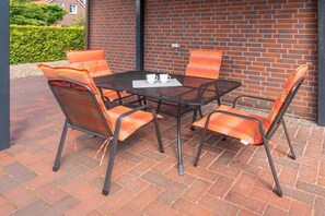 Ein Patio-Tisch mit vier Stühlen, eine Ziegelwand und ein Hecken im Hintergrund.