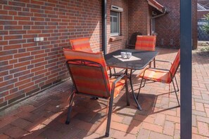 Une terrasse extérieure avec un mur en briques, des chaises en métal et une table sur laquelle sont posées deux tasses.