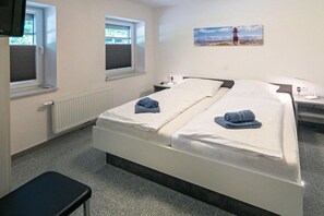 Ein Hotelzimmer mit Doppelbett, zwei Nachttischen, einer Bank, einem Fenster und einem Bild an der Wand.