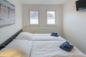 Een hotelkamer met twee bedden, een radiator en een aan de muur bevestigde televisie.