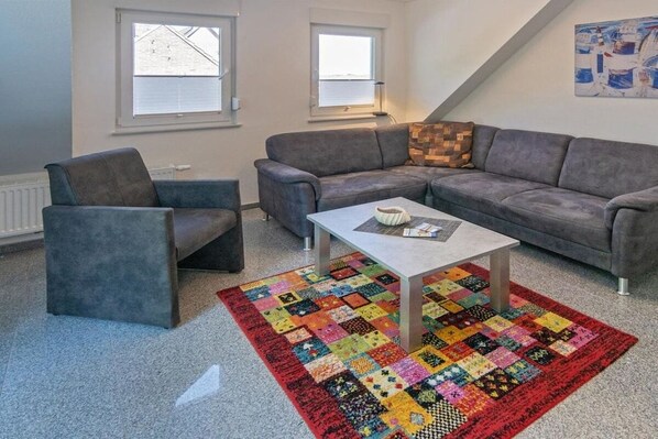 Ein Wohnzimmer mit einem grauen Sofa, einem passenden Sessel, einem Couchtisch und einem farbenfrohen Patchwork-Teppich.