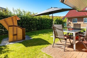 Eine Terrassengaststätte mit Tisch und Stühlen, ein Korbsessel und ein großer Sonnenschirm.
