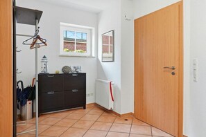 Um corredor com radiador, um armário preto, uma porta de madeira e uma janela com vista para um prédio de tijolos.