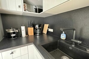 A kitchen with a black countertop, a stainless steel sink, a coffee maker, a kettle, and a bottle of hand soap. - Holiday apartment with 1 bedroom (Wangerooge)