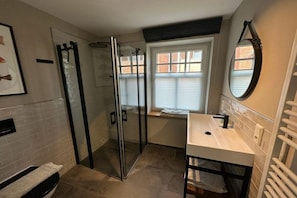 A bathroom with a glass-enclosed shower, a white sink, a mirror, and a window with blinds. - Holiday apartment with 1 bedroom (Wangerooge)