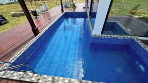 Una piscina rectangular con borde de azulejos, rodeada por una terraza de madera.