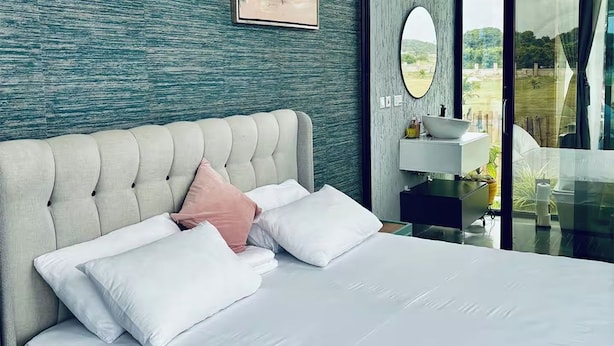Un dormitorio moderno con cabecera capitonada, ropa de cama blanca y vista a un jardín a través de una puerta de cristal.