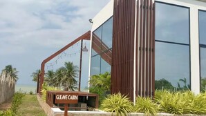 Una cabaña llamada 'GLEAVE CABIN' con una pared de piedra, listones de madera y vistas a la playa.
