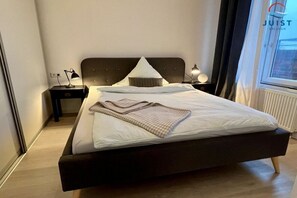 Een moderne slaapkamer met een groot bed, twee nachtkastjes, een raam met gordijnen en een radiator.