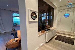 A modern interior with a window, a framed picture, a radiator, and a door with a circular window. - Apartment 107 - Beautiful Juist Woman (Juist)