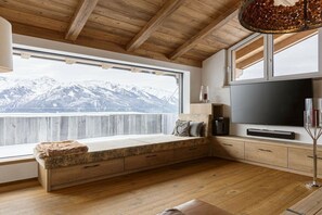 A room with a wooden ceiling, a large window with a mountain view, a built-in bench with storage, a flat-screen TV, and a tall floor lamp. - Apartment in Mittersill with swimming pool (Mittersill)