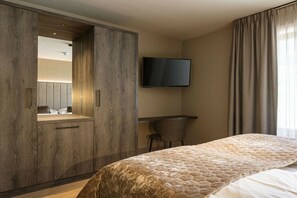 Hotellihuone, jossa on suuri sänky, peilillä varustettu vaatekaappi, seinälle asennettu televisio ja työpöytä tuolilla.