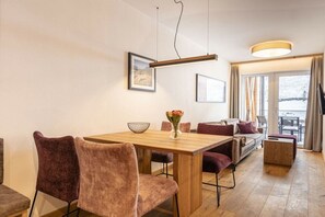 A modern dining area with a wooden table and chairs, a vase with flowers, and a sofa with cushions. - Holiday apartment with 1 bedroom (Rauris)