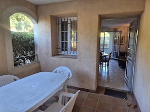 Uma área de pátio com mesa e cadeiras, uma janela com grades de metal e vista para o interior.