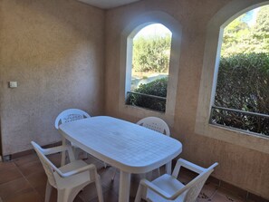 A room with a white table and chairs, a window with a view of greenery, and a textured wall. - 1-Bedroom Apartment in JARDINS DU GOLFE with Community Pool (Le Plan-de-la-Tour)