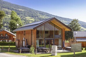 A wooden lodge with a sloped roof, large windows, and a patio area with tables and chairs. - Cabin with 1 bedroom (St. Georgen am Kreischberg)