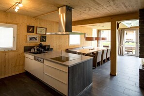 A modern kitchen with a central island, wooden walls, and a dining area with a long table and chairs. - Cabin with 1 bedroom (St. Georgen am Kreischberg)