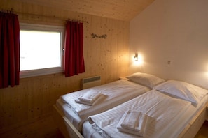 A room with two beds, a window with red curtains, and a wall-mounted light fixture. - Cabin with 1 bedroom (St. Georgen am Kreischberg)