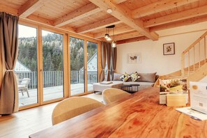 Een houten interieur met een grote schuifglazen deur die uitkomt op een balkon, een bank en een houten tafel met documenten.