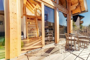 Eine Holzterrasse mit Gartenmöbeln, ein Glastür-Eingang und ein sichtbarer Innenraum mit Bett und Tisch.