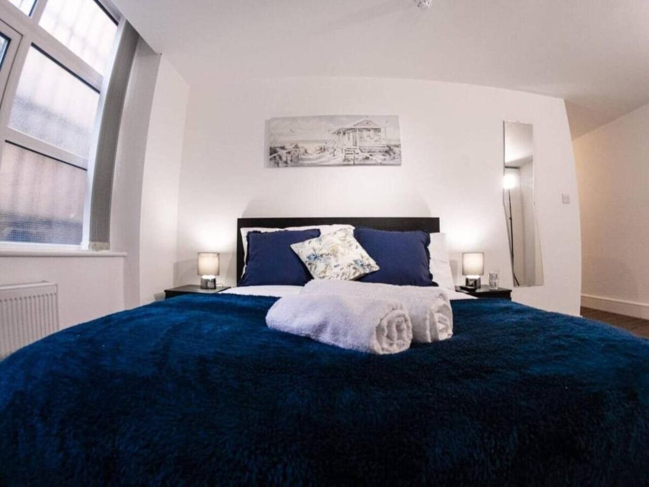 A bedroom with a large bed, two bedside tables, a window, and a wall-mounted artwork.