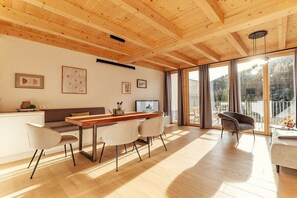 A modern interior with a wooden ceiling, a dining area with a long table and chairs, a sofa, and a large sliding glass door leading to a balcony. - Chalet #7 with 3 bedrooms and sauna (Niederwölz)