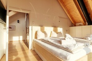 Une chambre à coucher avec un lit en bois, une literie blanche et un plafond en pente avec des poutres apparentes.