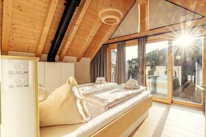 A bedroom with a wooden ceiling, a bed with white linens, a white wardrobe, and a large window with a view of the outdoors. - Chalet #7 with 3 bedrooms and sauna (Niederwölz)