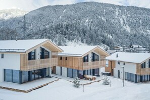 A modern building with a wooden facade and large windows, surrounded by snow-covered trees and mountains.