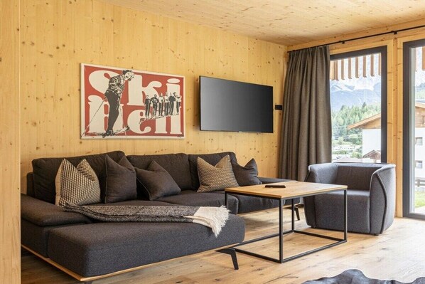 A modern living room with a sofa, a coffee table, and a television on the wall.