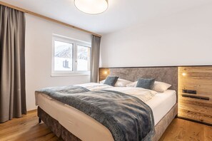 A bedroom with a bed, a window, curtains, and a wooden headboard. - Holiday apartment with 2 bedrooms (Rauris)
