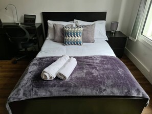 A neatly made bed with a purple blanket and two rolled towels, a laptop on a bedside table, and a lamp on the nightstand. - Sav Apartments Rutland Leicester -Studio (Leicester)