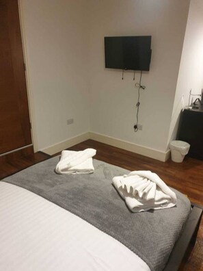 Ein Hotelzimmer mit Bett, einem flachbildfernseher an der Wand und einem kleinen Nachttisch mit Lampe.