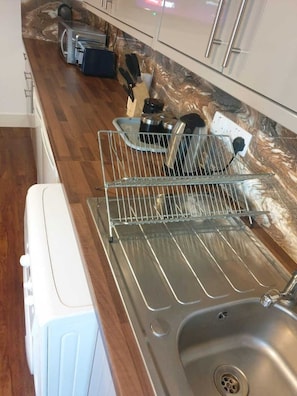 Cozinha com pia de aço inoxidável, escorredor de louça e eletrodoméstico branco.
