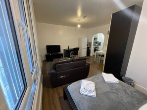 En moderne stue med sofa, et fladskærms-tv og et spiseområde med bord og stole.