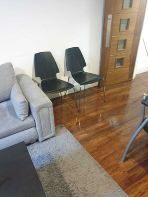 Ein Zimmer mit einem grauen Sofa, zwei schwarzen Stühlen, einer Holztür und einem dunklen Tisch.
