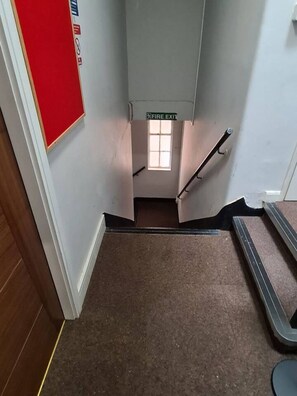 Een trap met een bordje voor de branddeur, een rood nooduitgangsbord en een raam aan de bovenkant van de trap.