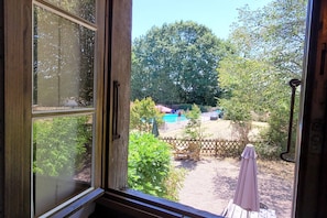 Blick durch ein offenes Fenster in einen Hinterhof mit Pool, Holzzaun und Gartenmöbeln.