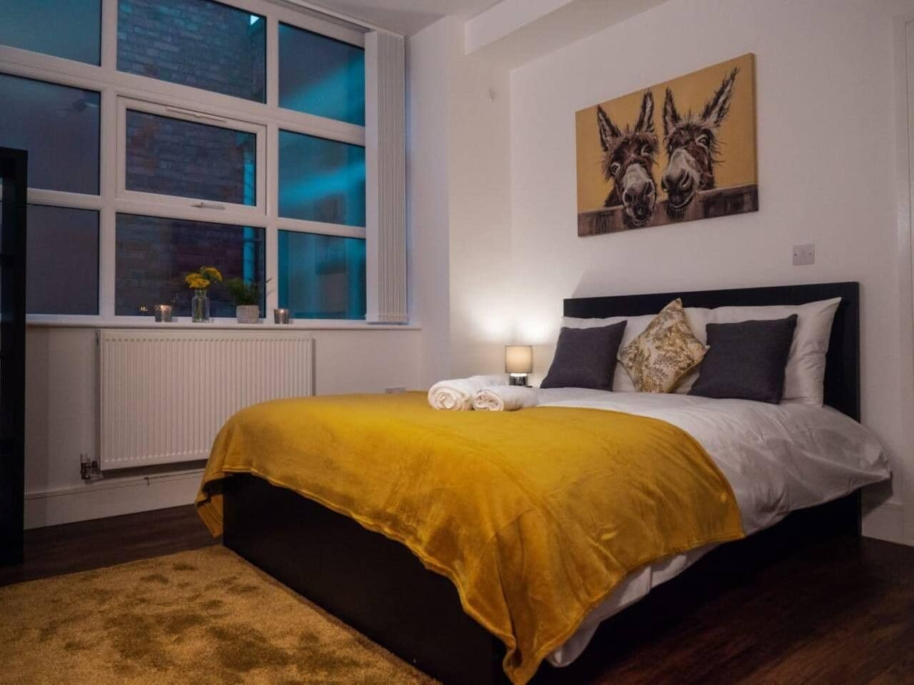 A bedroom with a bed, a window, a radiator, and a painting on the wall.