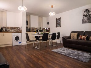 A modern living room with a dining area, a sofa, and a kitchen in the background. - Sav Rutland Town Centre-3 Bed Apartment (Leicester)